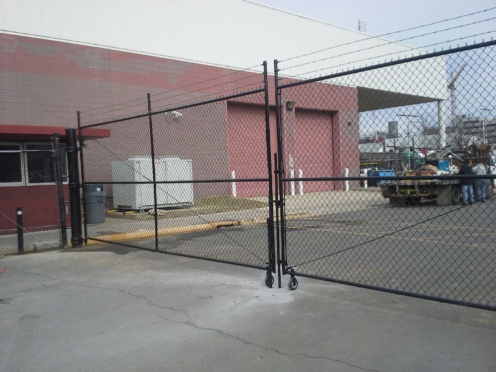A steel and composite material fence with chain-link and wire mesh surrounds an outdoor building against a bright sky.