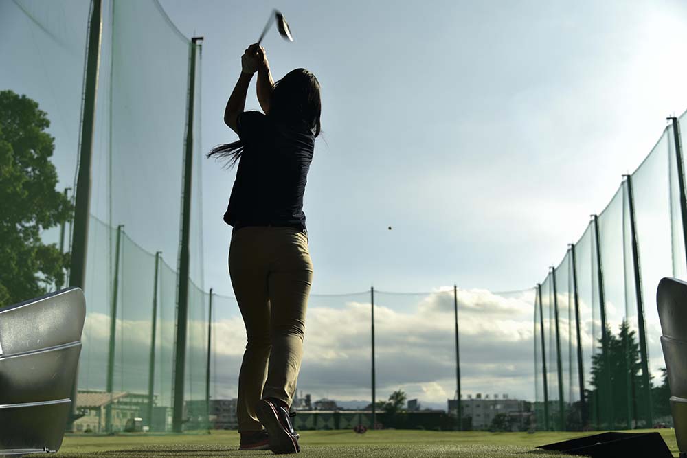 golf-netting A person is playing a sport of golf outdoors on a grassy field surrounded by trees and clouds in the sky.