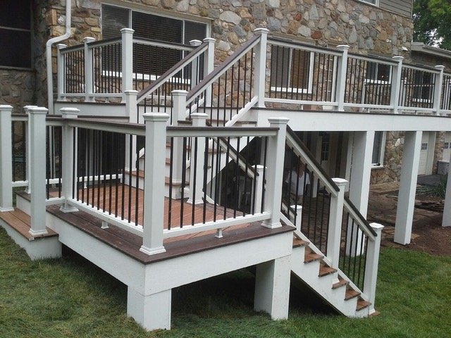 White deck 2 A wooden house with a porch and deck stands on the property, surrounded by grass and featuring an outdoor staircase with a handrail and balusters.