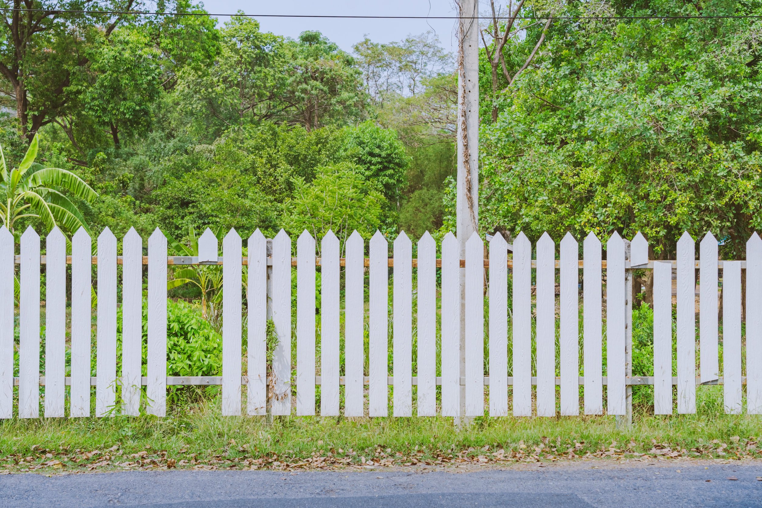 Old white wooden fence with a broken board at the roadside area Old white wooden fence with a broken board at the roadside area
